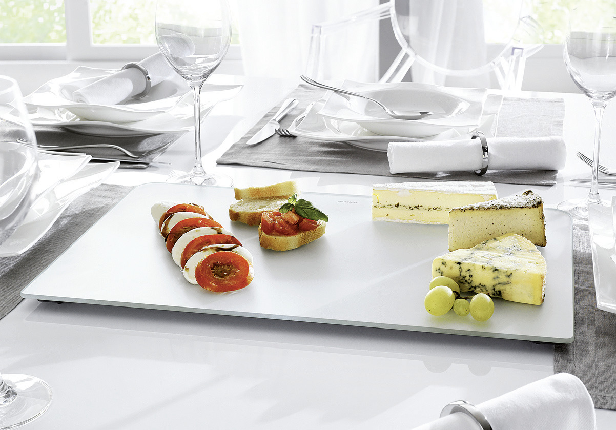 A white cutting board made of glass on which various dishes are placed
