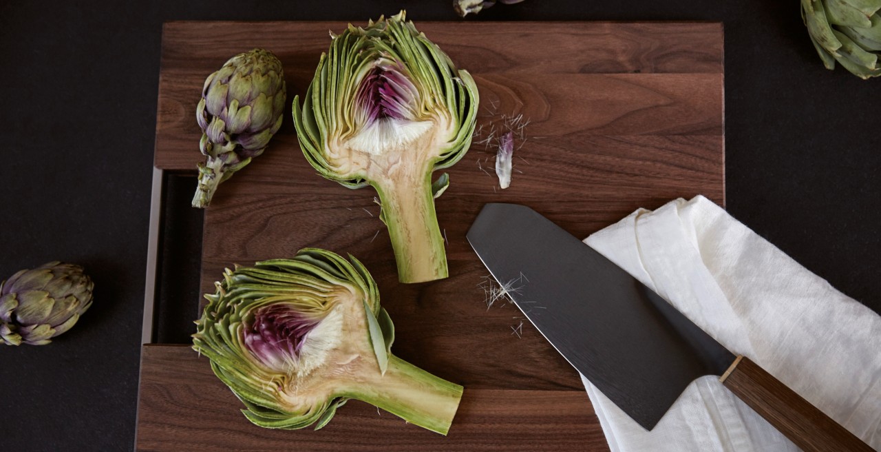 A halved artichoke on a dark chopping board