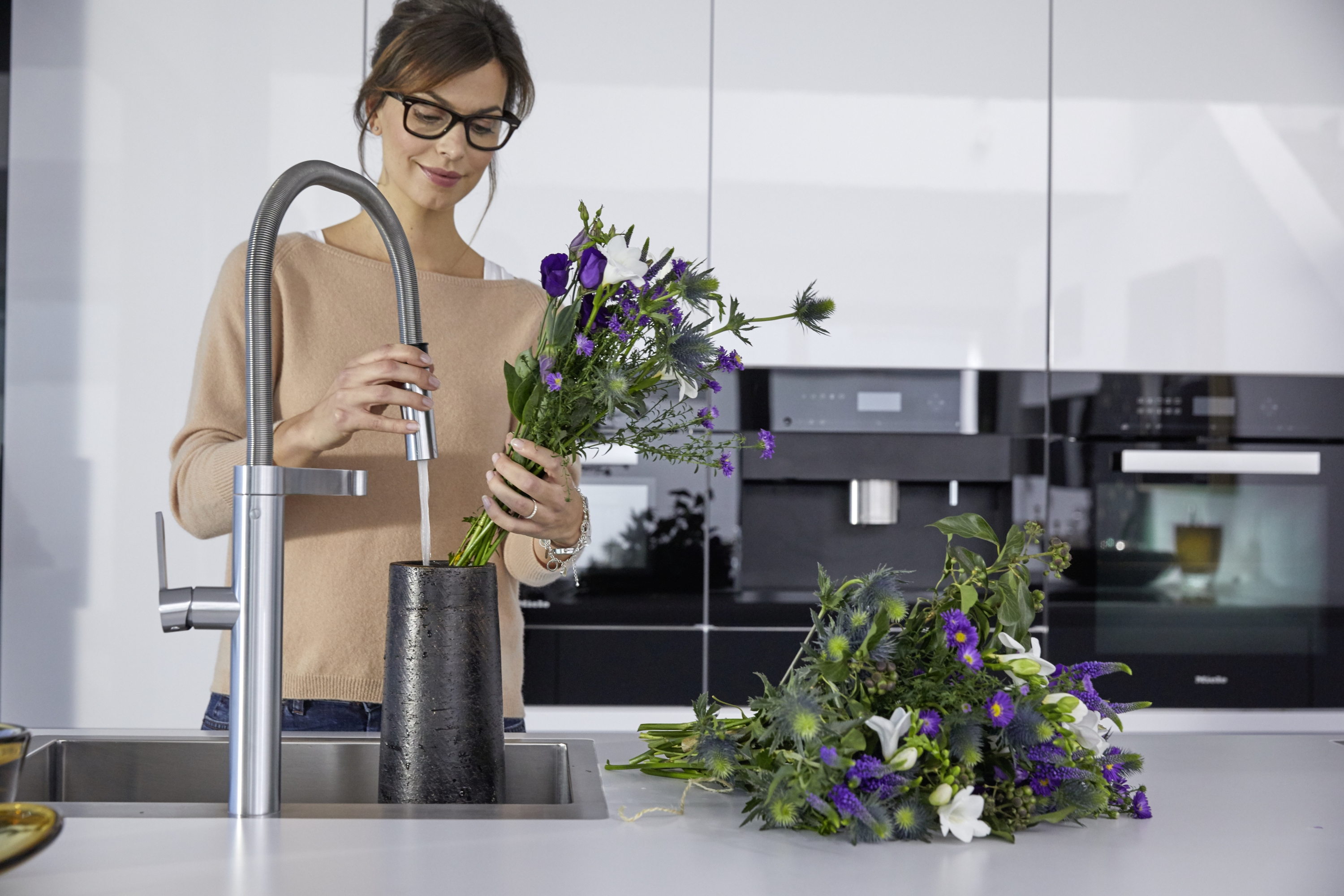 a woman is arranging flowers in a BLANCO stainless steel sink