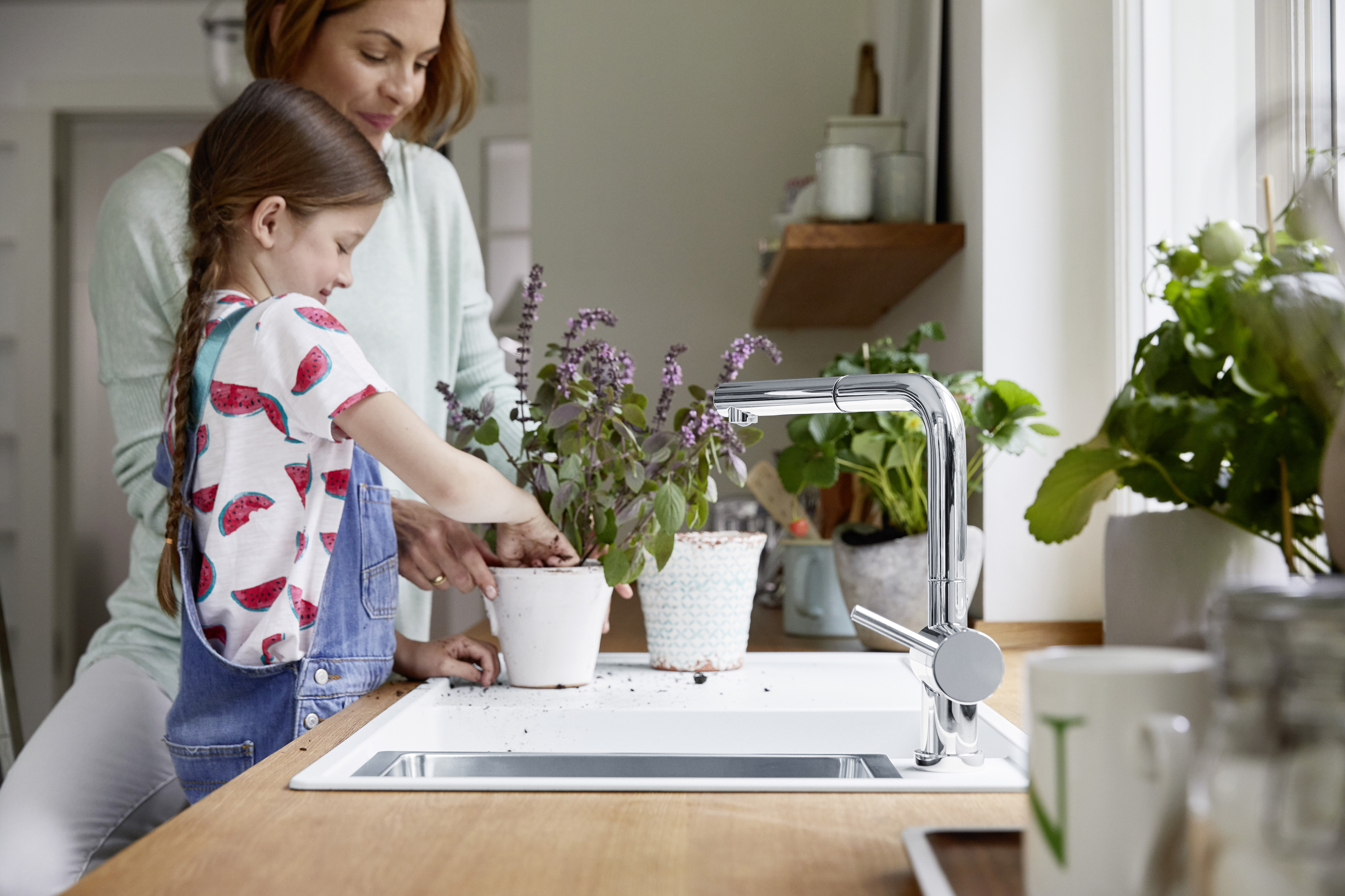 a girl and a woman are repotting a plant on a white silgranit sink