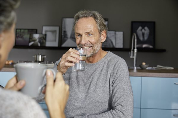 A man drinks a glass of water and smiles